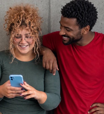 Smiling woman looking at her phone while a man in a red T-shirt leans on her shoulder