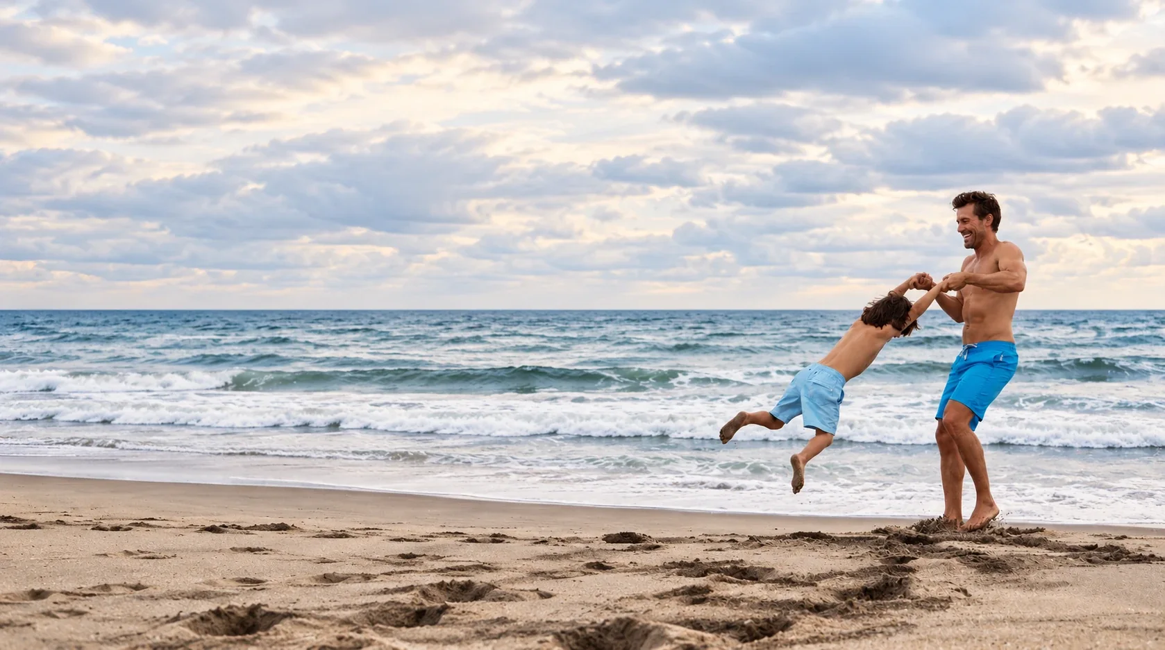 Father swinging his son by the hands at the edge of the sea