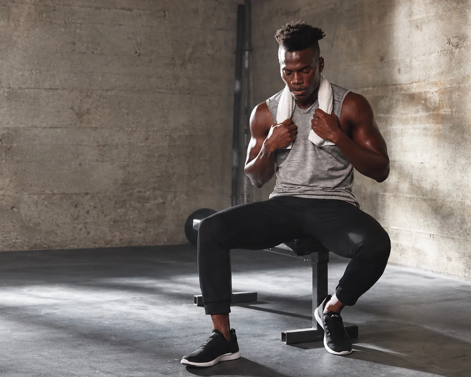 Man resting on a weight bench with a towel around his neck in a concrete gym